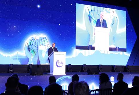A person standing at a podium with a large screen